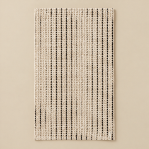 Serviette de bain nid d’abeille à rayures dépliée sur fond beige